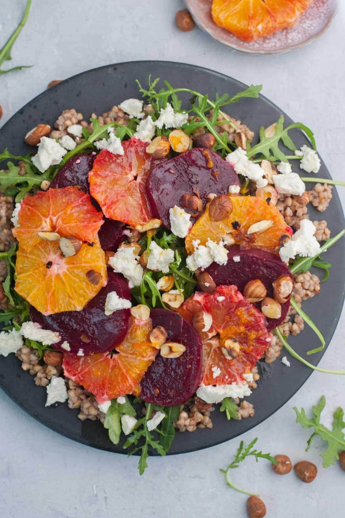 Buckwheat salad with beets, oranges, arugula, and feta cheese on a black plate.