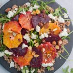 Buckwheat salad with beets, oranges, arugula, and feta cheese on a black plate.