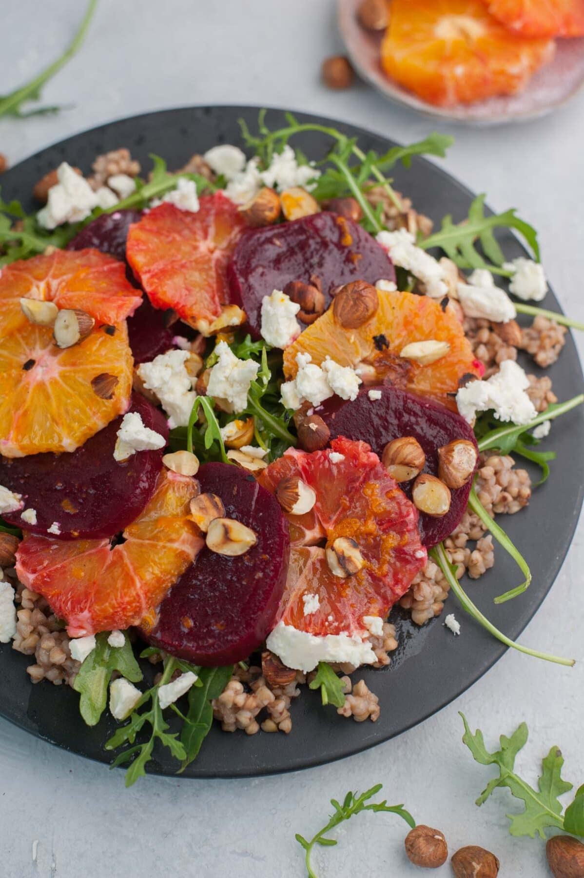 Buckwheat salad with beets, oranges, arugula, and feta cheese on a black plate.