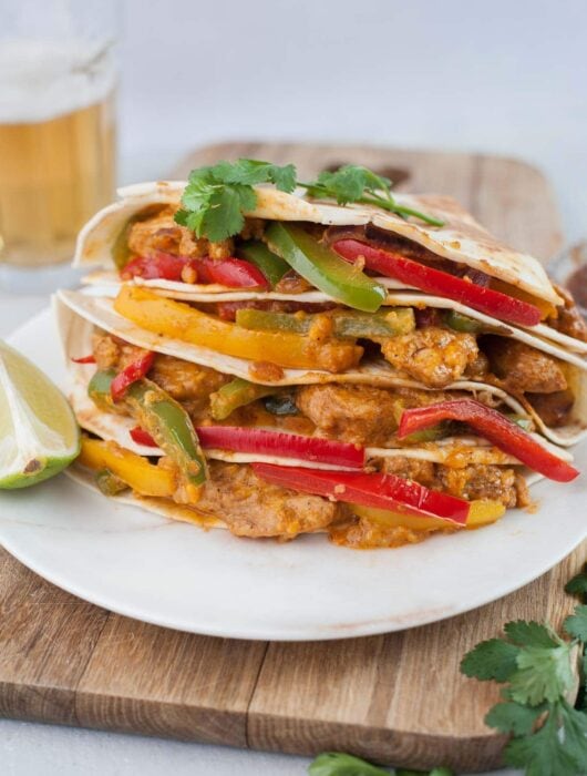 Chicken fajita quesadillas on a wooden boards topped with cilantro leaves.