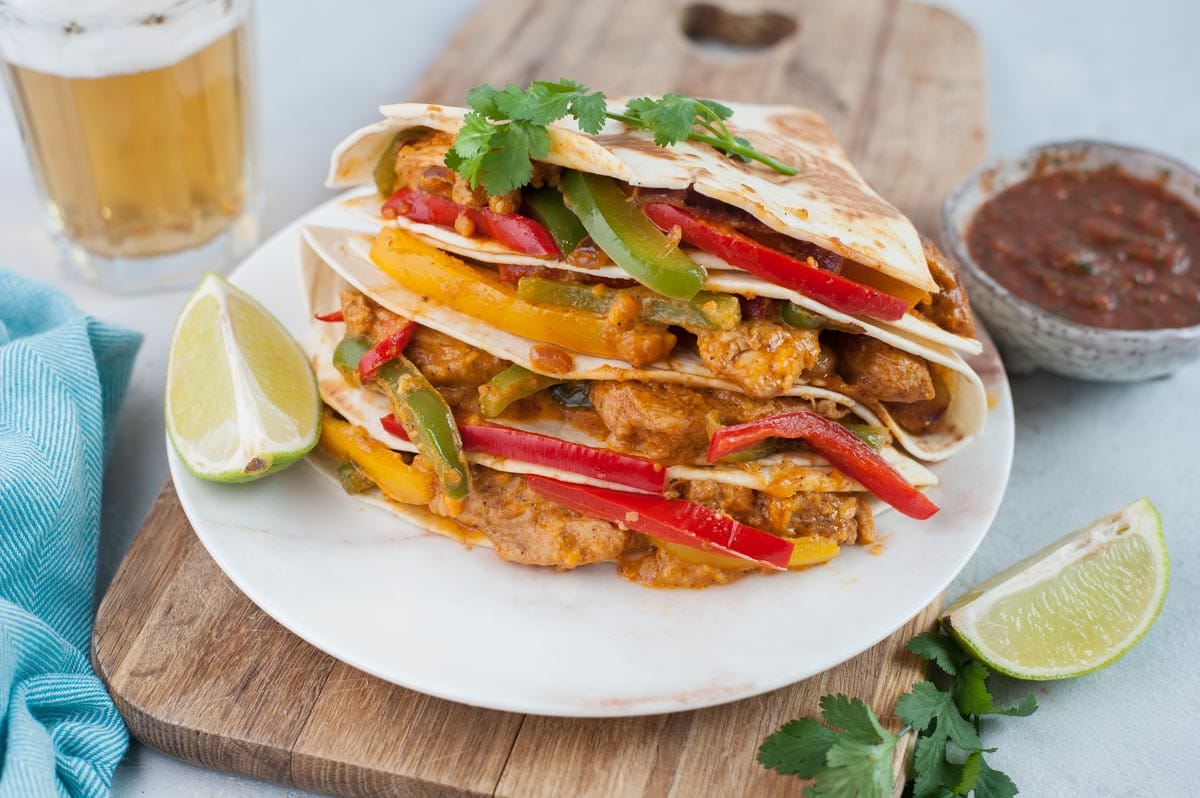 Chicken fajita quesadillas on a white plate. Cilantro leaves and lime quarters on the side.