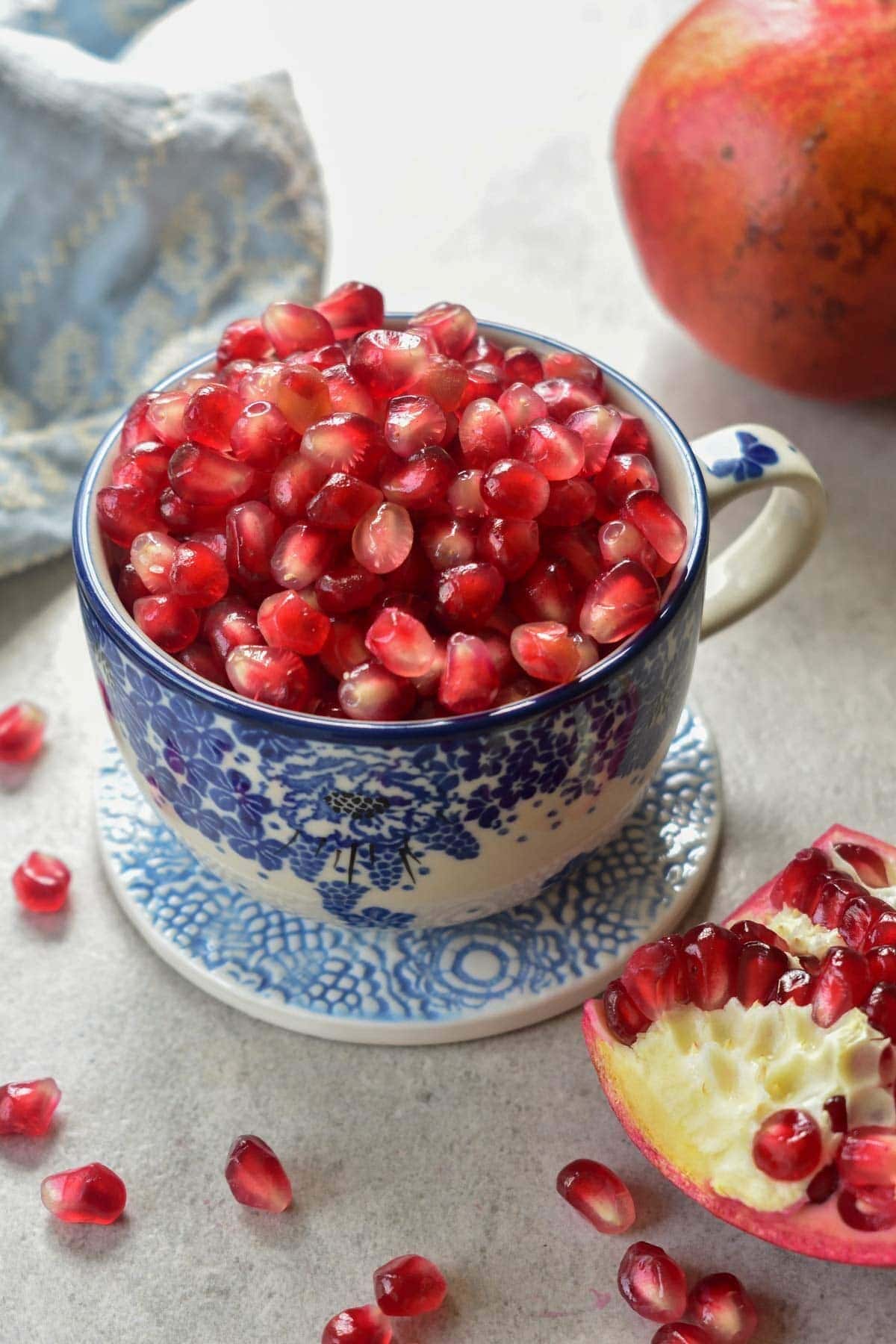 Pomegranate seeds in a blue cup. Pomegranate in the background.