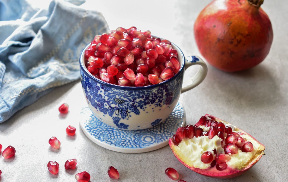 Pomegranate seeds in a blue cup. Pomegranate in the background.