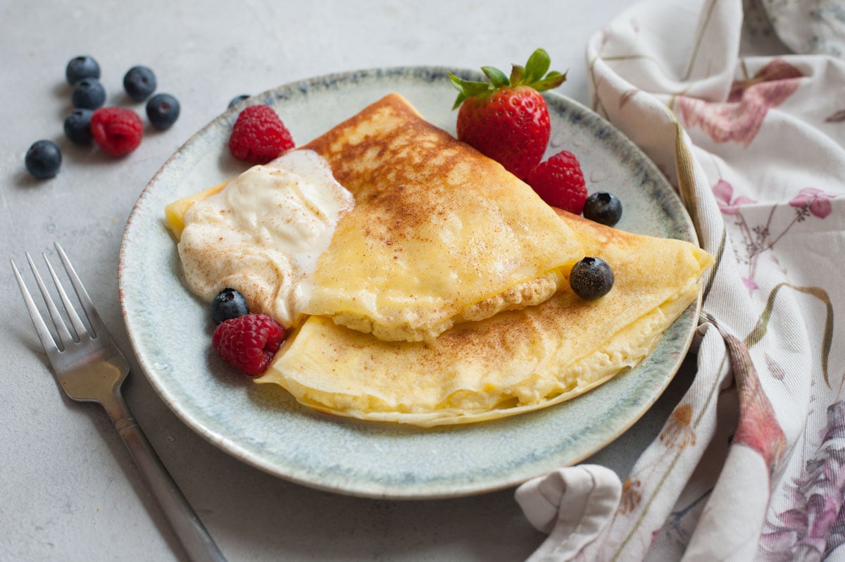 Nalesniki with cheese filling on a green plate. Whipped cream and berries on the side.