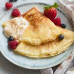 Nalesniki with cheese filling on a green plate. Berries and whipped cream on the side.