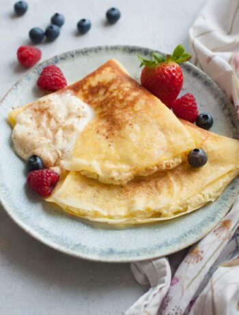 Nalesniki with cheese filling on a green plate. Berries and whipped cream on the side.