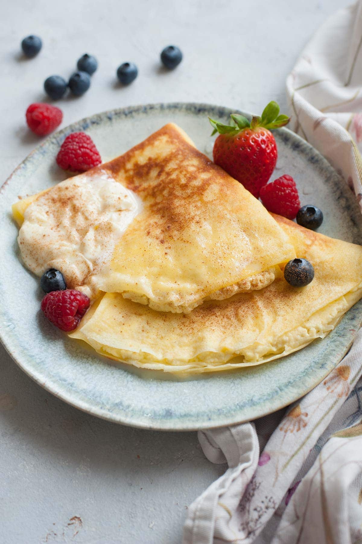 Nalesniki with cheese filling on a green plate. Whipped cream and berries on the side.