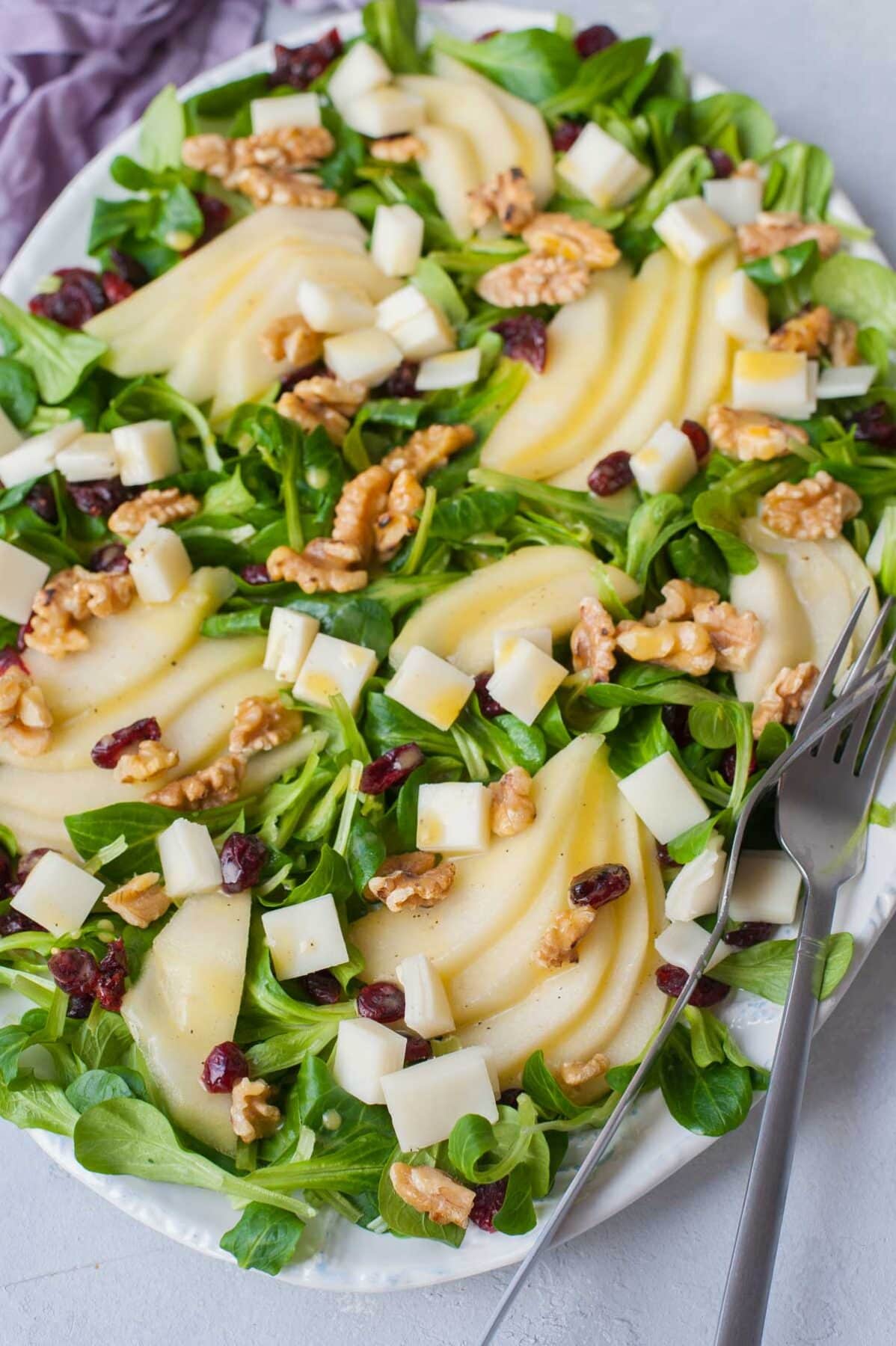 Pear walnut salad with cranberries and goat cheese on a white plate.