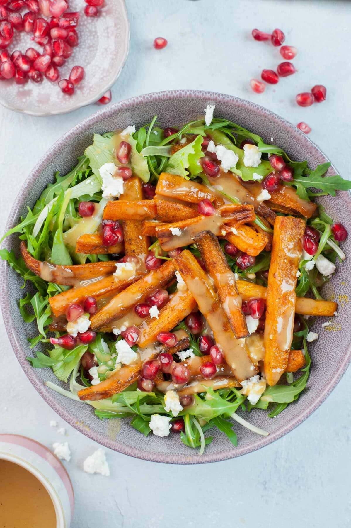 Roasted carrot salad with pomegranate and peanut butter lemon dressing in a violet bowl.