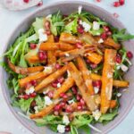 Roasted carrot salad with pomegranate, feta, and peanut butter lemon dressing in a violet bowl.