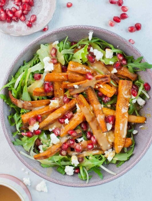 Roasted carrot salad with pomegranate, feta, and peanut butter lemon dressing in a violet bowl.