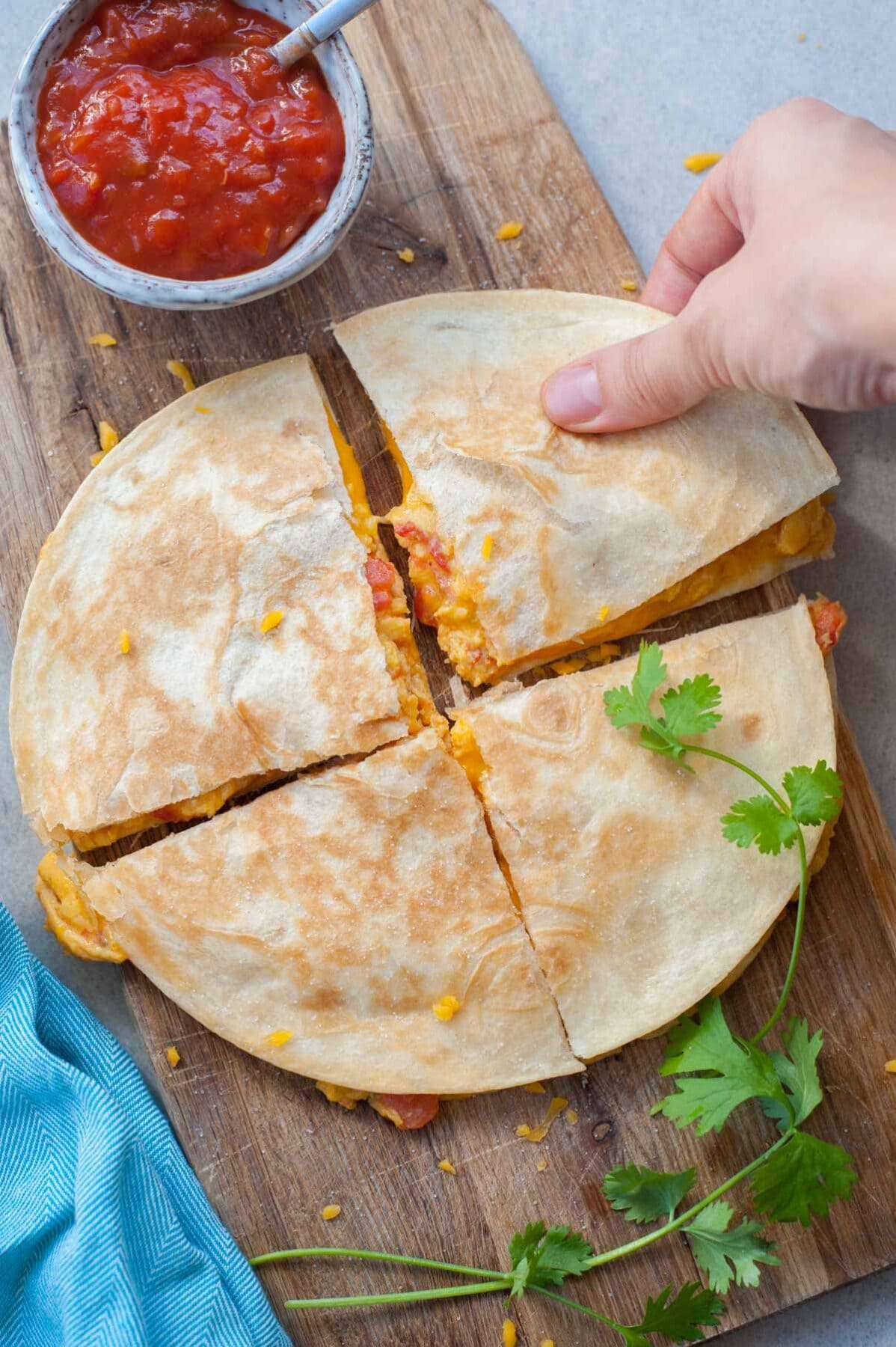 A hand is reaching for breakfast quesadilla on a wooden board.