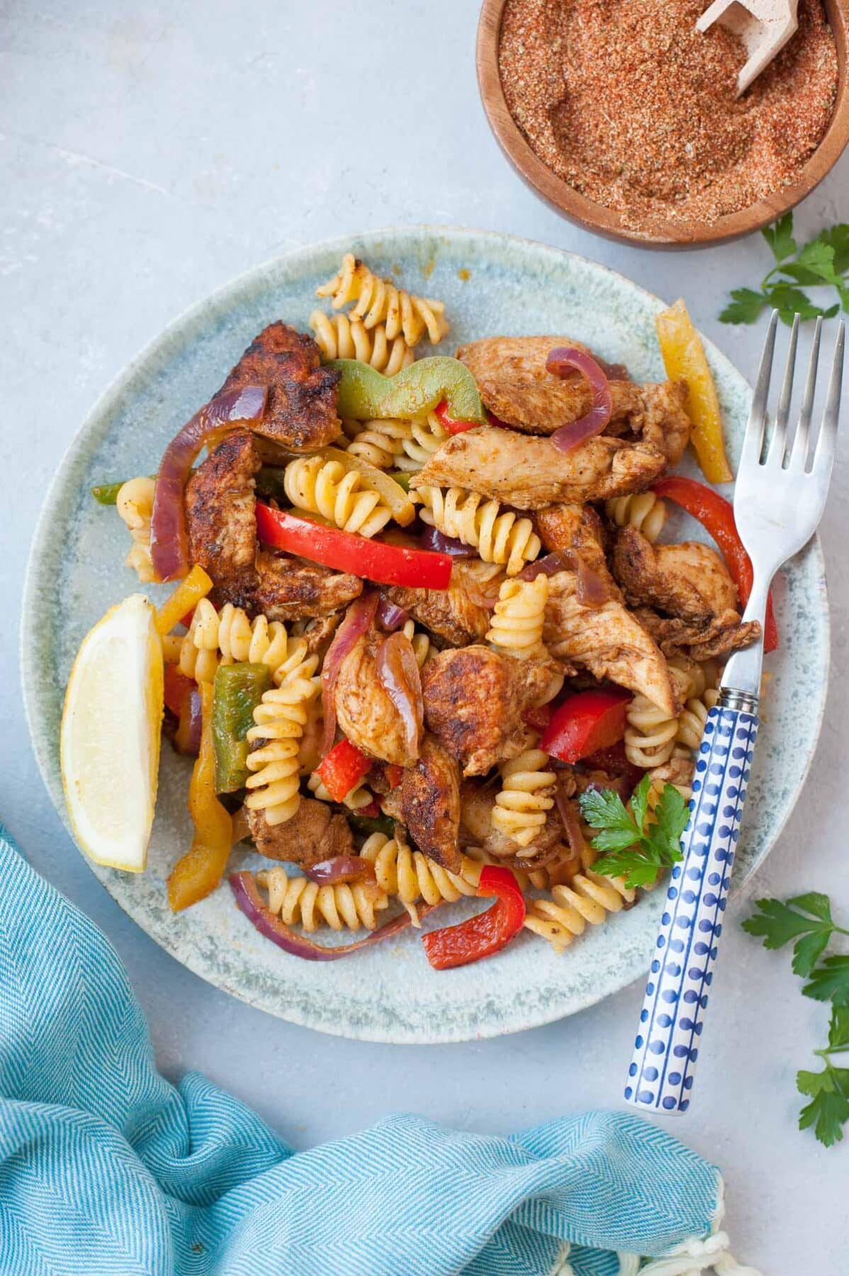 Chicken fajita pasta on a green plate, lemon quarter and fajita seasoning on the side.