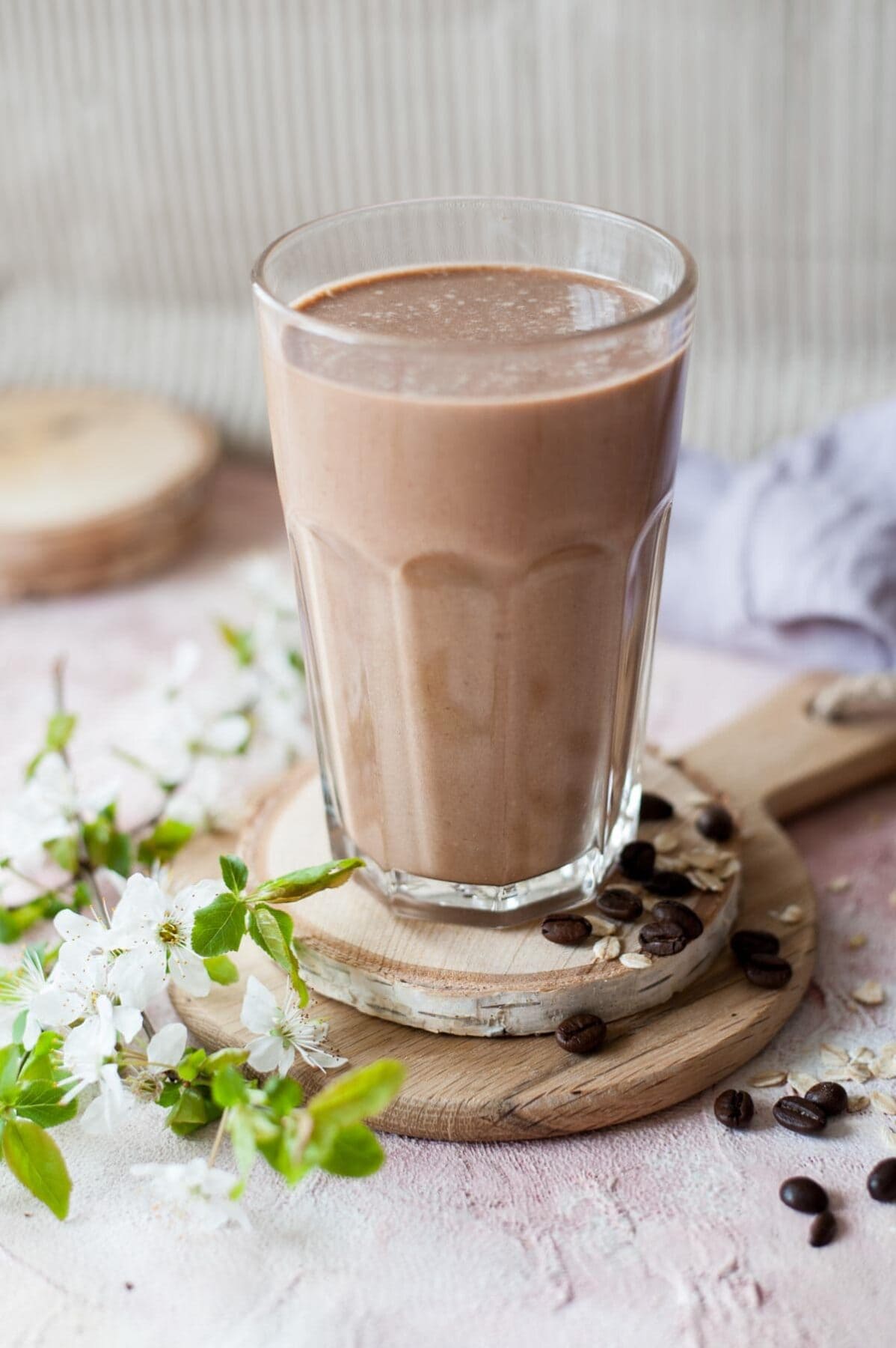 Coffee banana smoothie in a glas. Branch with flowers and coffee beans in the background.