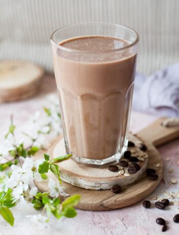 Coffee banana smoothie in a glass. Flowers and coffee beans on the side.