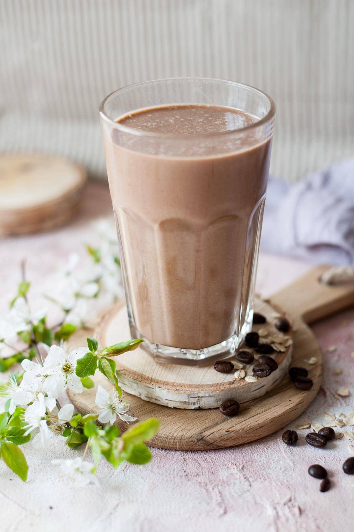 Coffee banana smoothie in a glass. Flowers and coffee beans on the side.