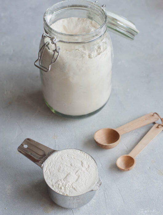 Measuring cup filled with flour, wooden spoons, jar with flour.