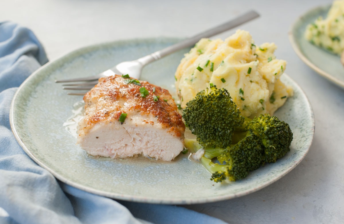 Cut in half parmesan mayo chicken breast on a green plate with mashed potatoes and broccoli.