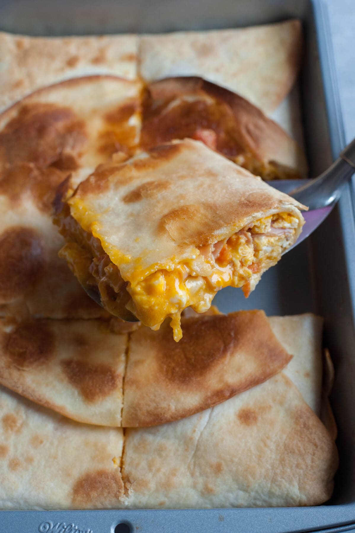 Sheet pan breakfast quesadillas in a pan with one serving on a spatula.