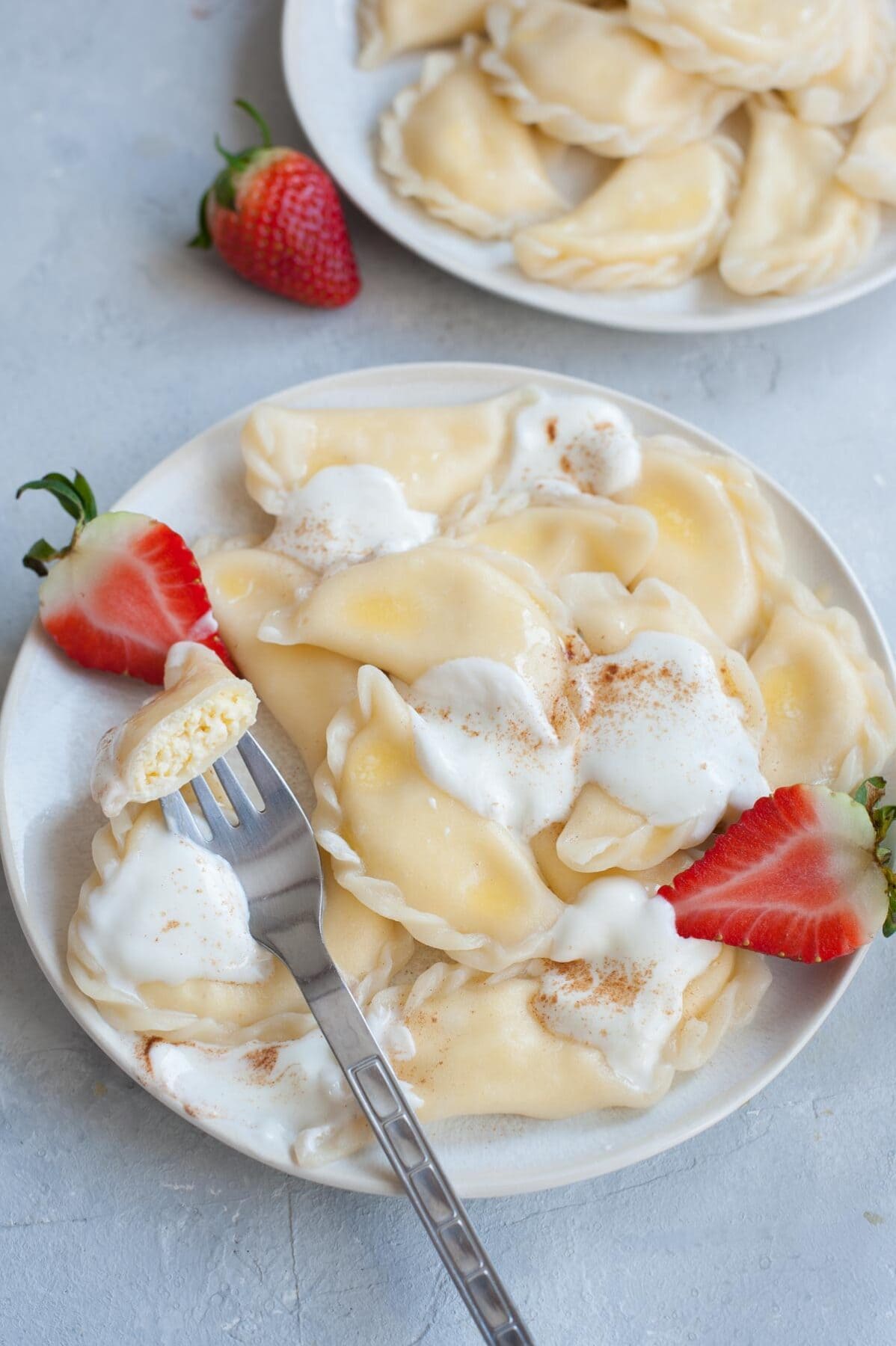 Sweet cheese pierogi on a white plate, topped with cream and strawberries.