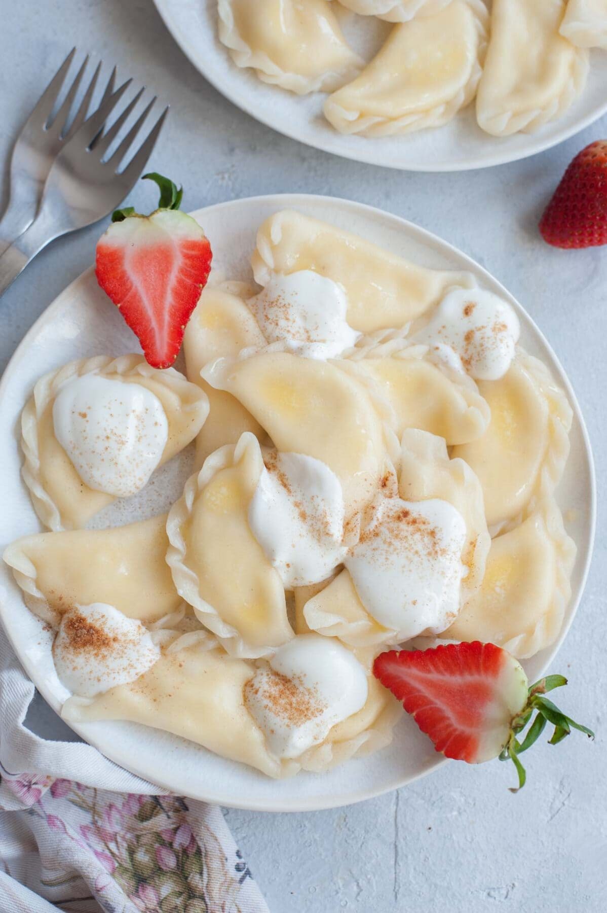 Sweet cheese pierogi on a white plate, topped with cream and strawberries.