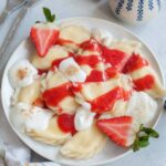 Sweet cheese pierogi on a white plate topped with strawberry sauce and whipped cream.