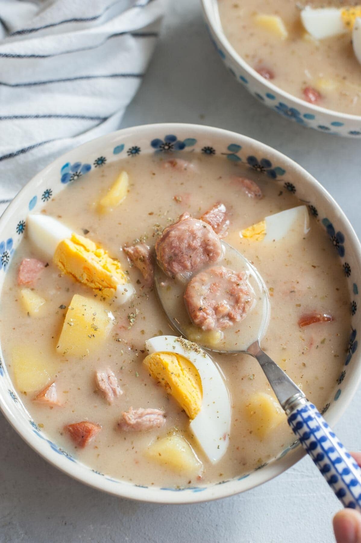 Żurek with kielbasa, eggs, and potatoes in a white-blue bowl.