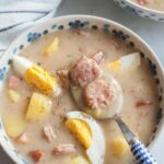 Żurek soup with potatoes and eggs in a white-blue bowl.