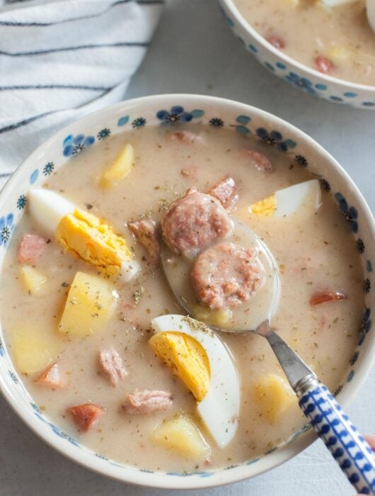 Żurek soup with potatoes and eggs in a white-blue bowl.