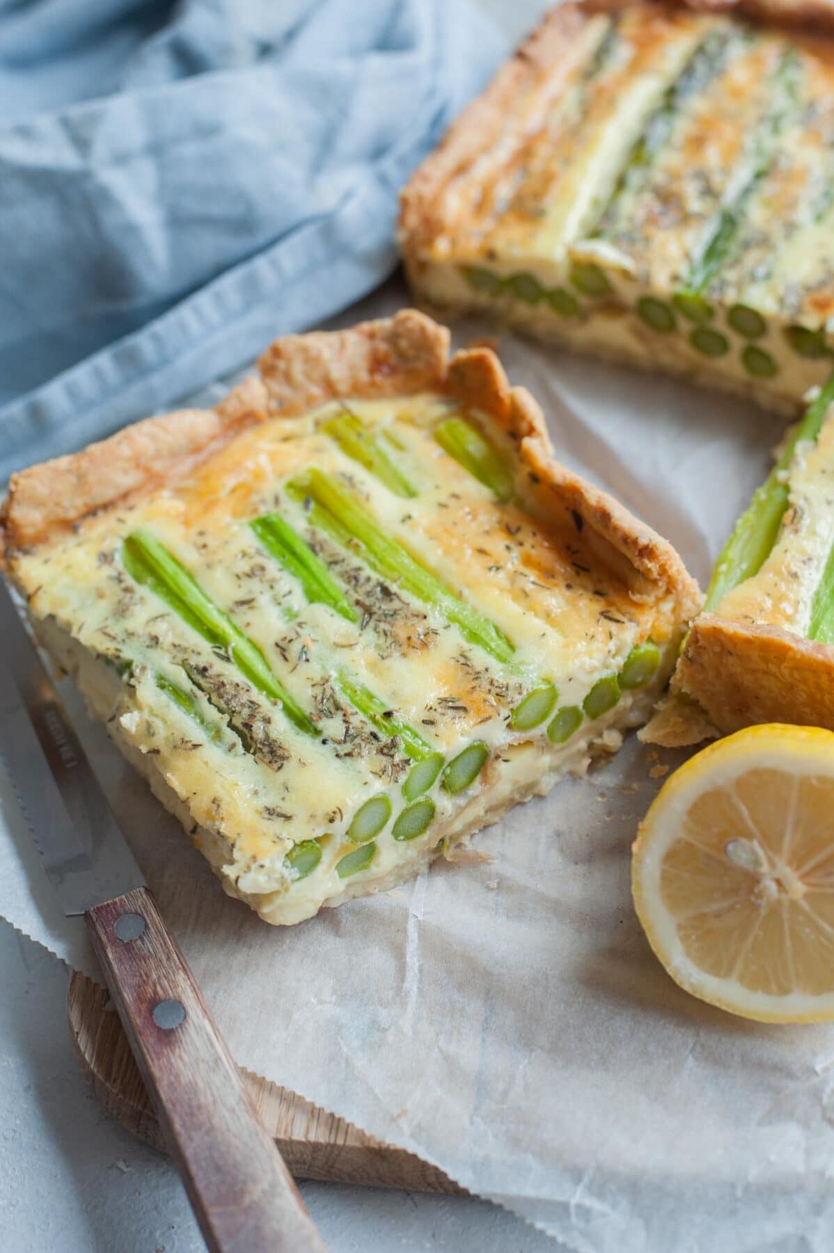 A close up picture of a piece of asparagus quiche. Whole quiche in the background.
