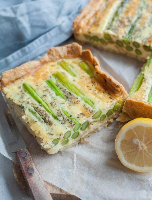 A piece of asparagus tart on parchment paper. Kitchen cloth and lemon in the background.