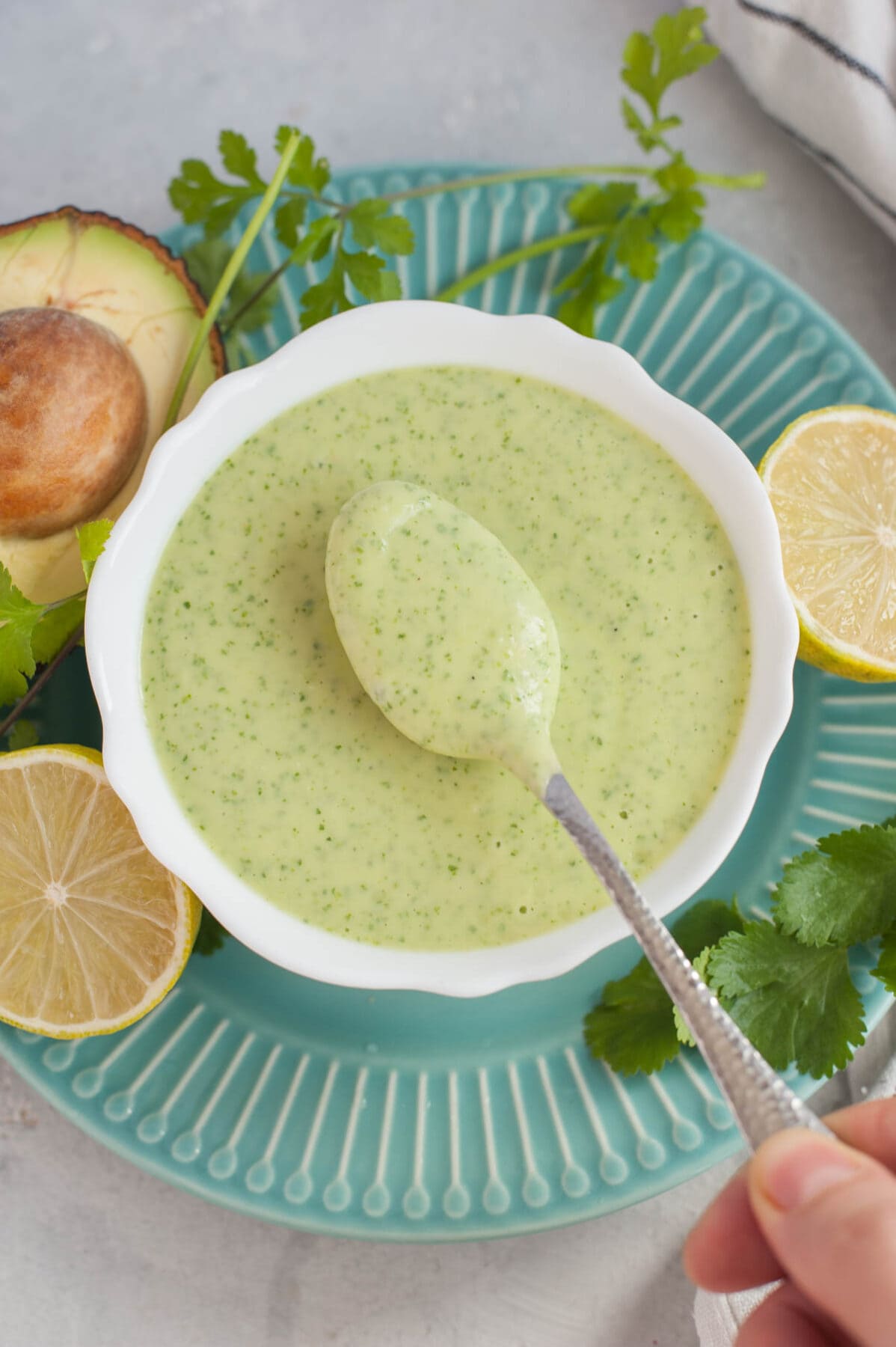 Avocado cilantro lime dressing in a white bowl and on a teaspoon.