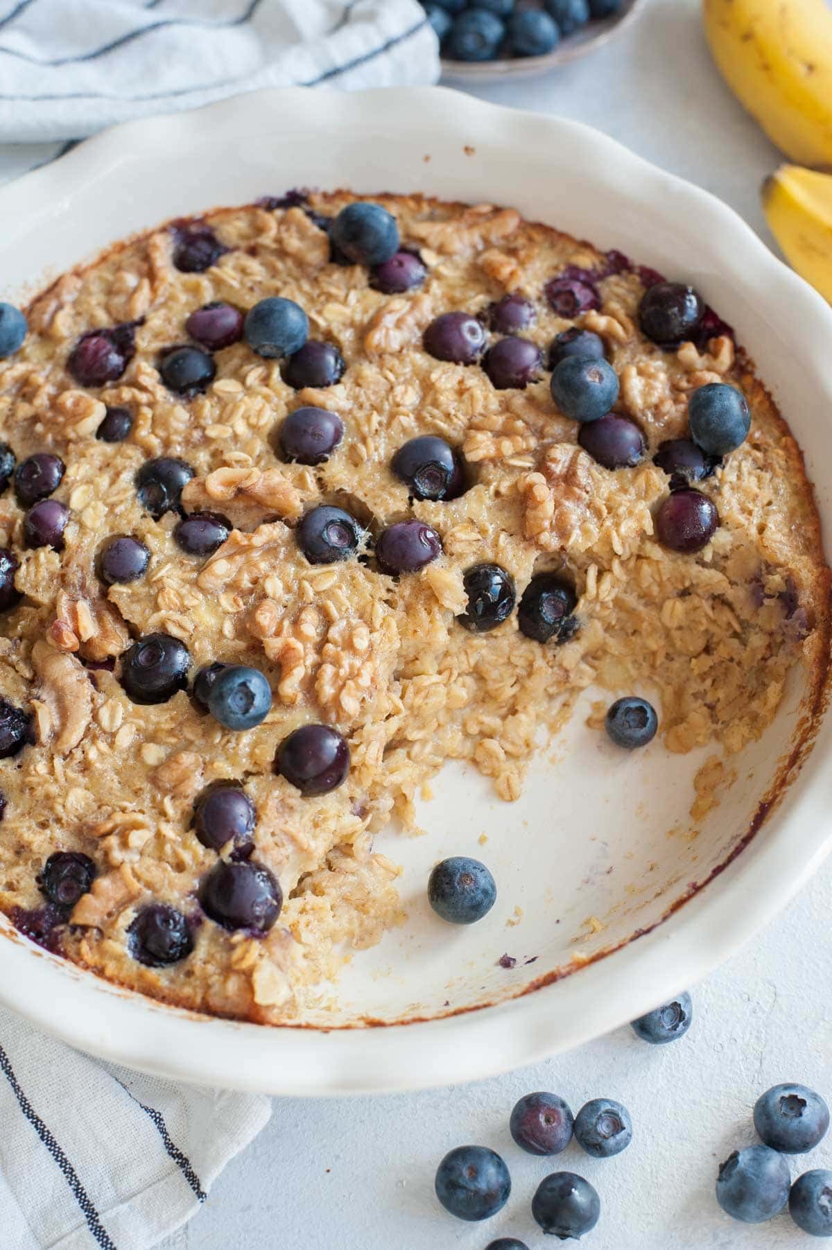 Banana blueberry baked oatmeal in a white baking dish with a serving missing.