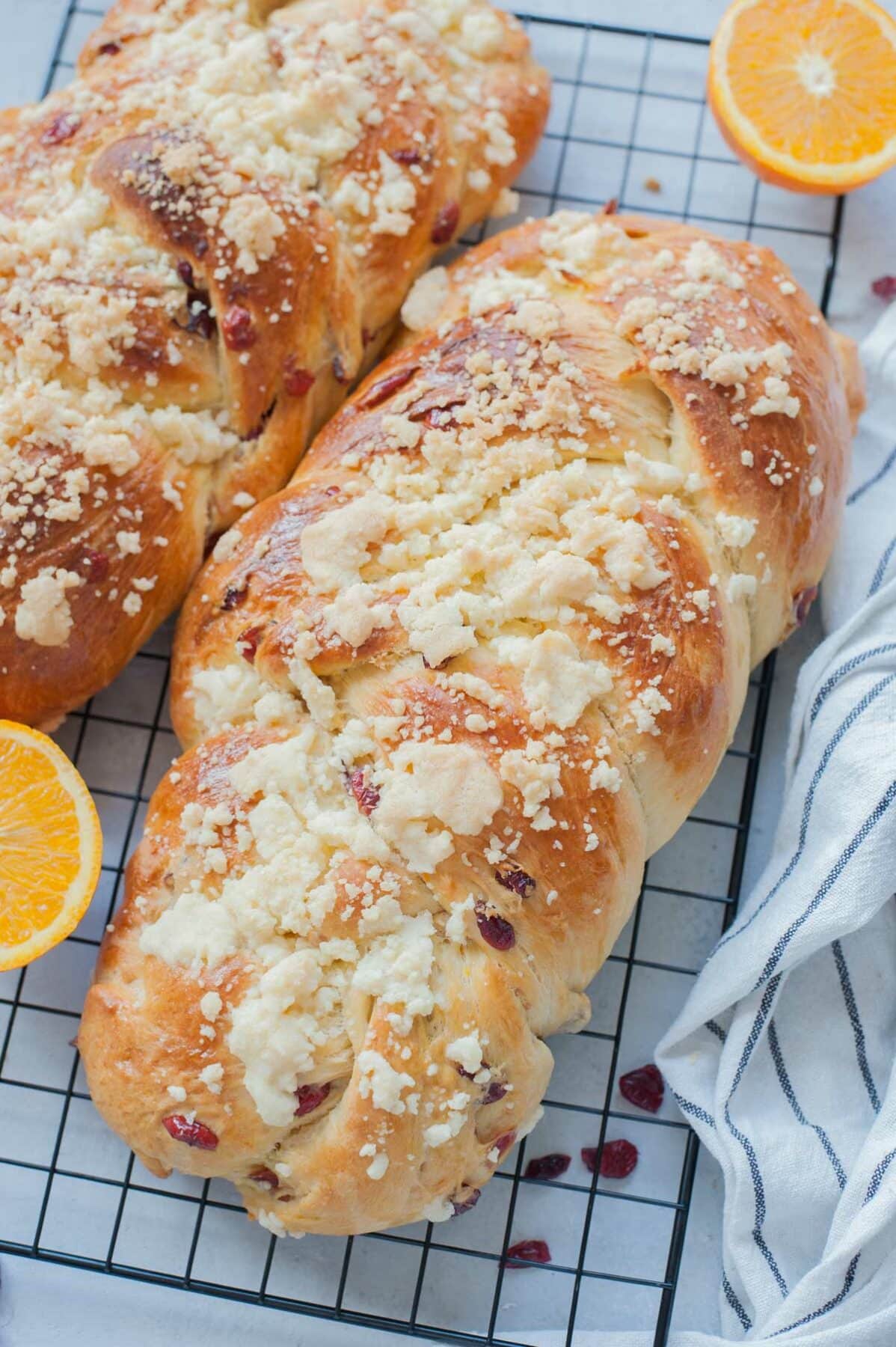 Two brioche breads on a cooling rack. Dried cranberries and oranges in scattered around.