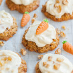 Carrot cake cookies with cream cheese frosting on a piece of parchment paper topped with marzipan carrots and nuts.