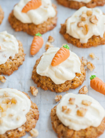 Carrot cake cookies with cream cheese frosting on a piece of parchment paper topped with marzipan carrots and nuts.