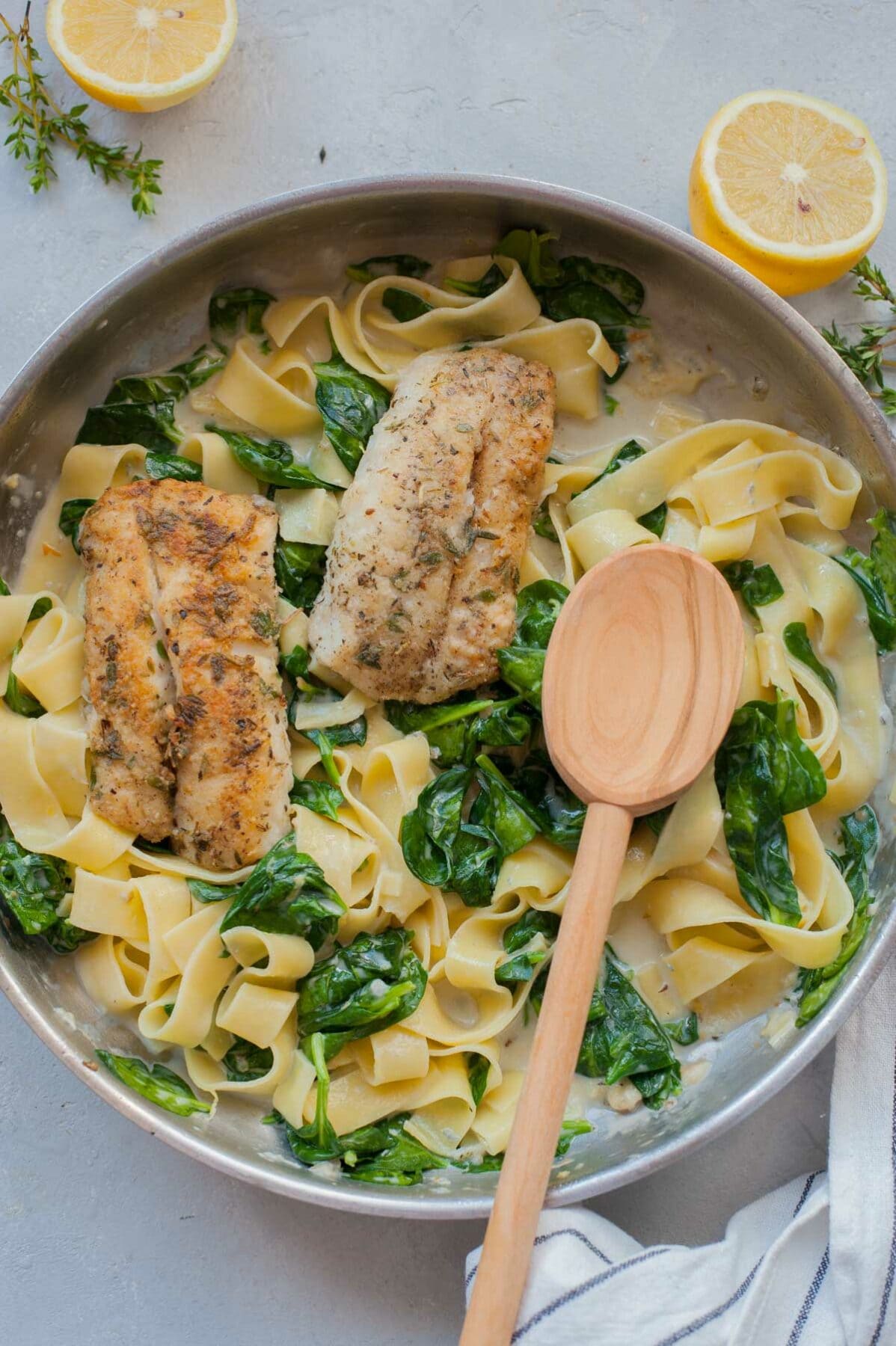 Gorgonzola spinach pasta and pa-fried fish in a frying pan.