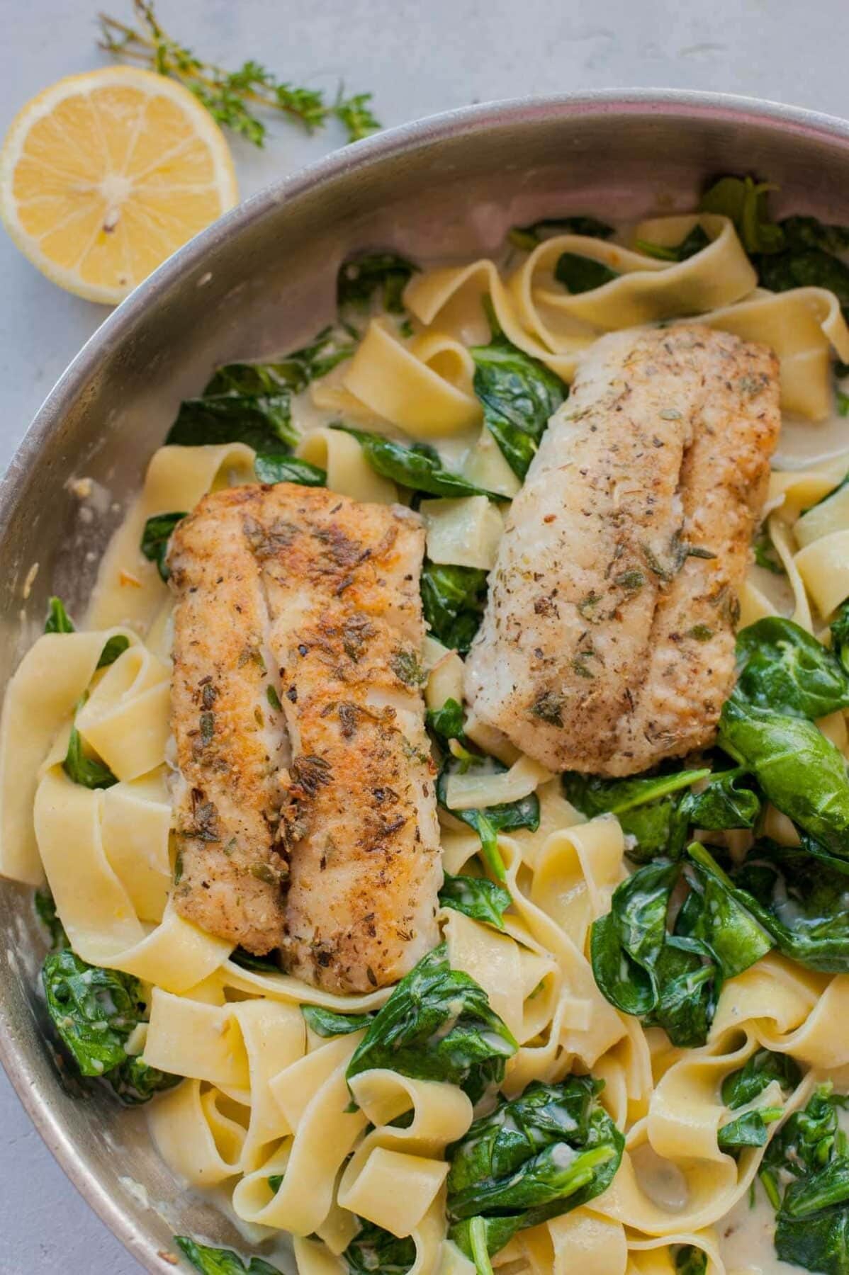 Gorgonzola spinach pasta and pa-fried fish in a frying pan.