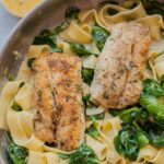 Gorgonzola spinach pasta with pan-fried fish in a frying pan.