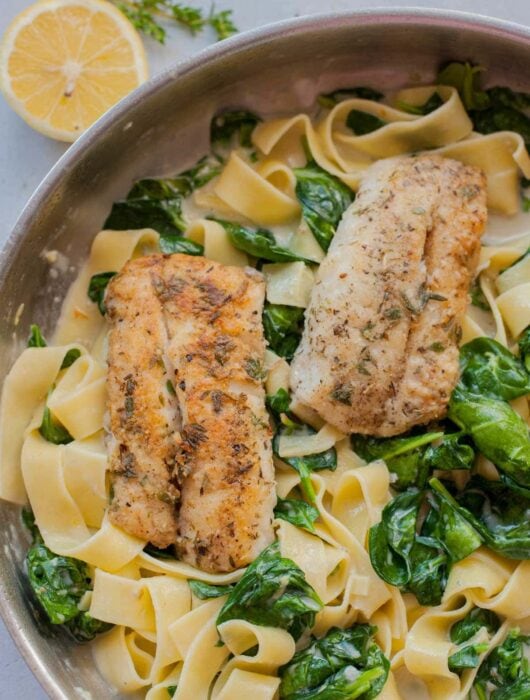 Gorgonzola spinach pasta with pan-fried fish in a frying pan.
