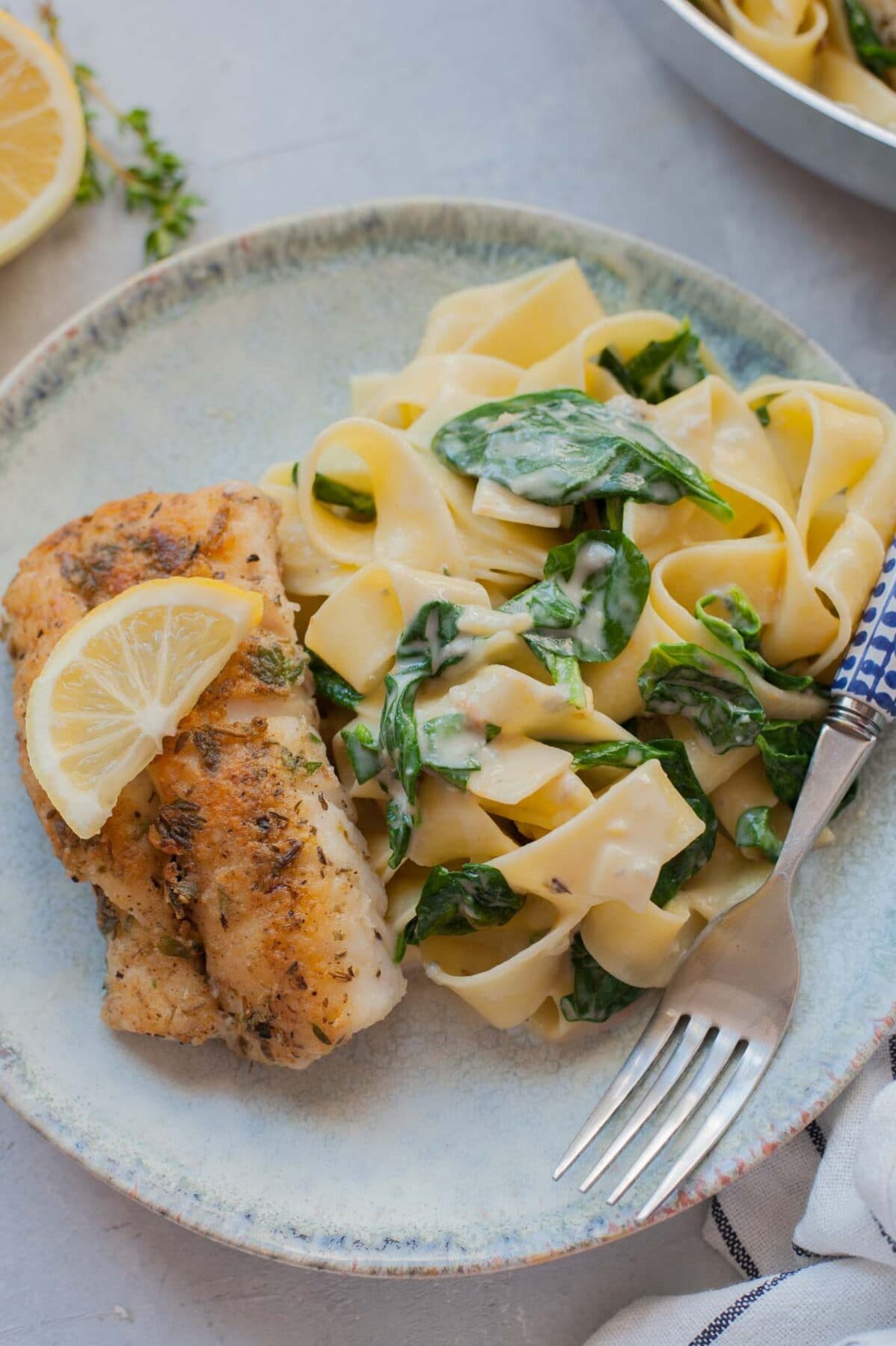 Gorgonzola spinach pasta and pa-fried fish on a green plate.