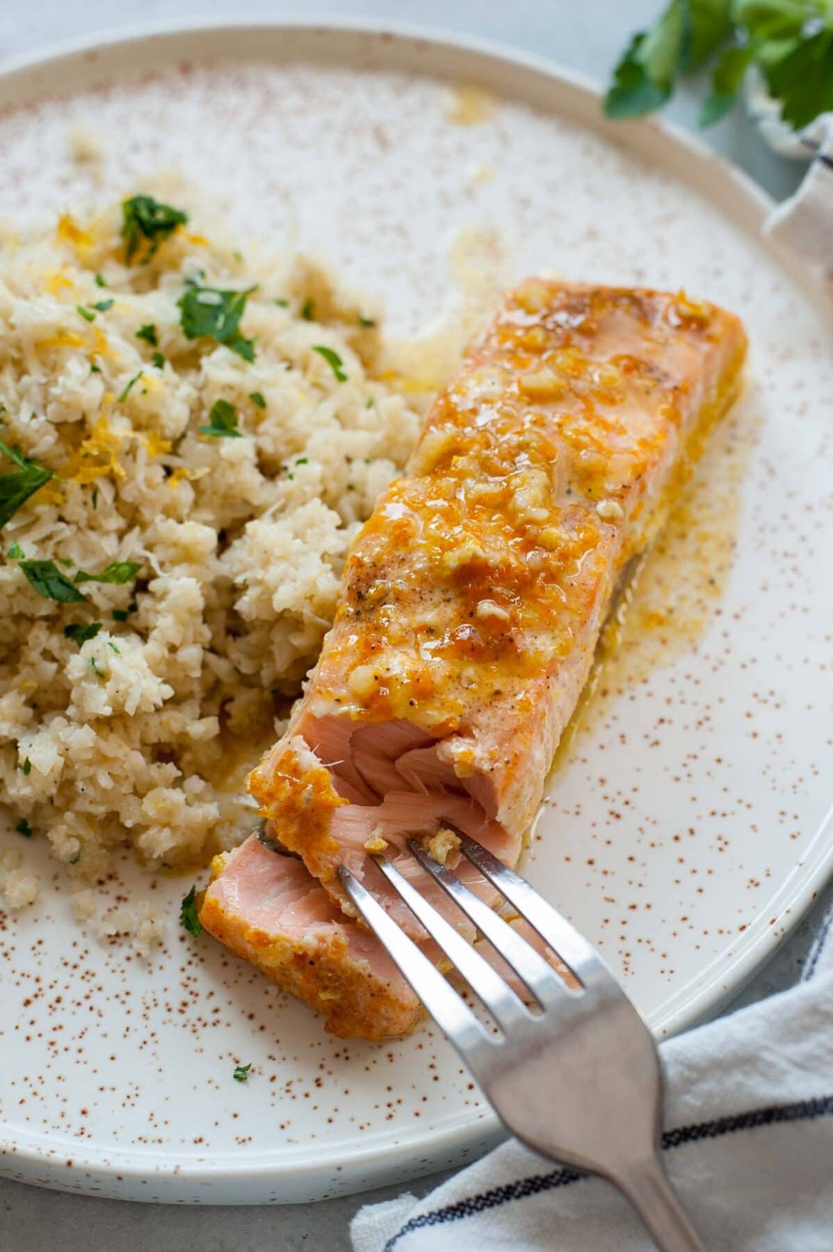 Orange maple salmon is being cut with a form on a white plate with a side of cauliflower rice.