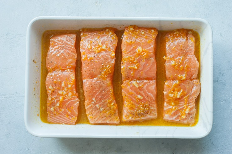 Salmon fillets with orange maple sauce in a white baking dish ready to be baked.