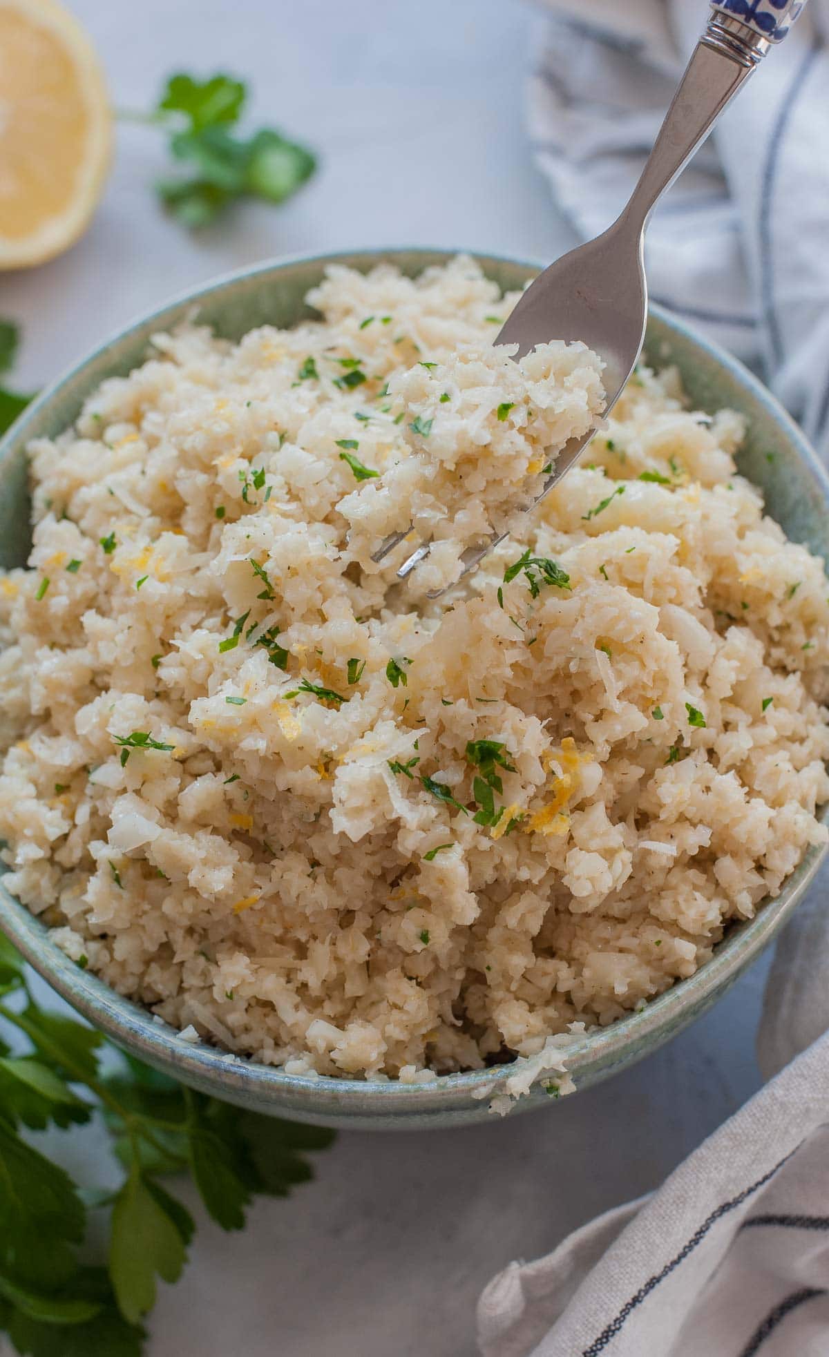 Parmesan cauliflower rice in a green bowl is being picked with a fork.