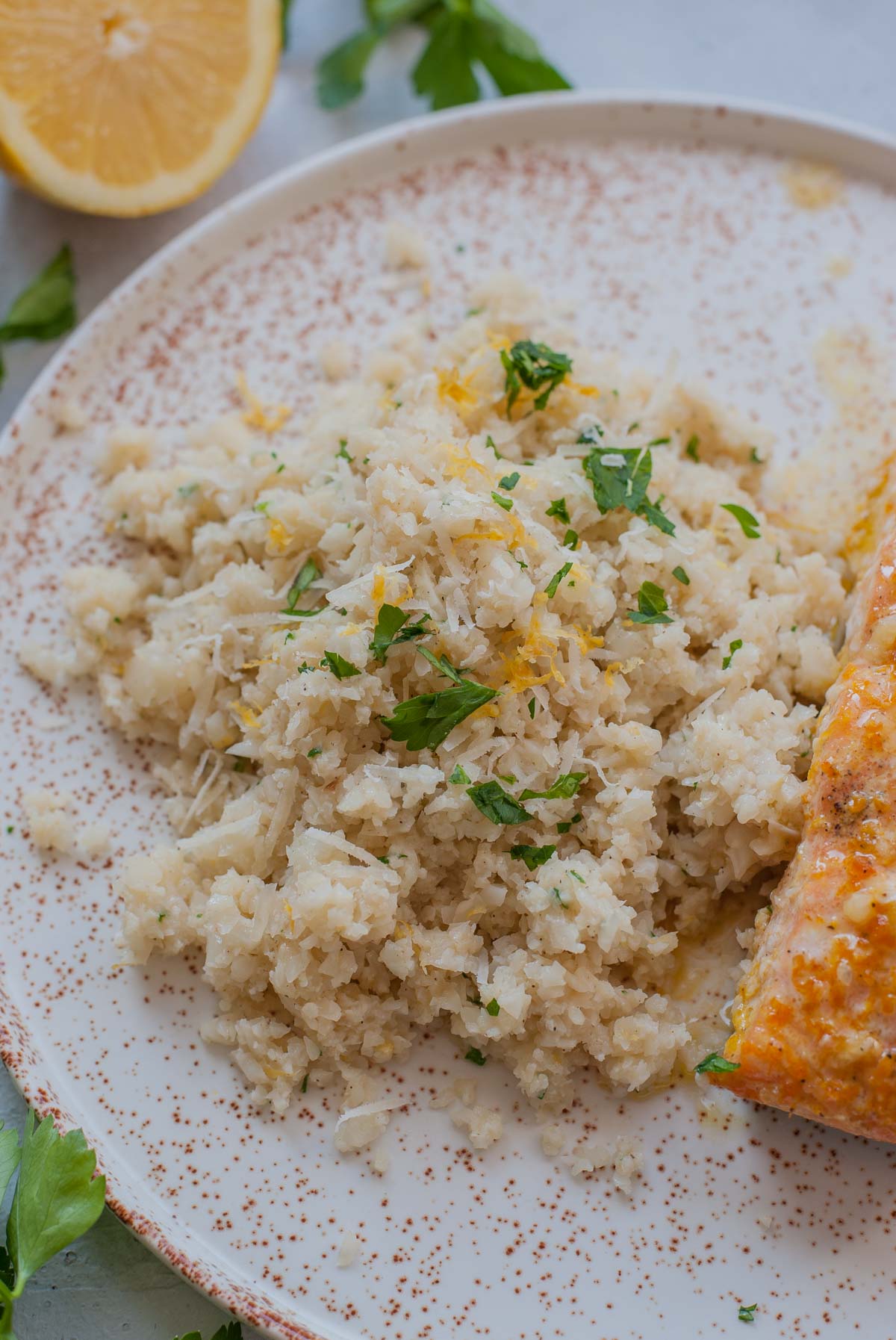 Parmesan cauliflower rice on a white plate served with salmon.