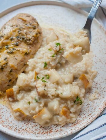 Pear risotto on a white plate with chicken breast on the side.