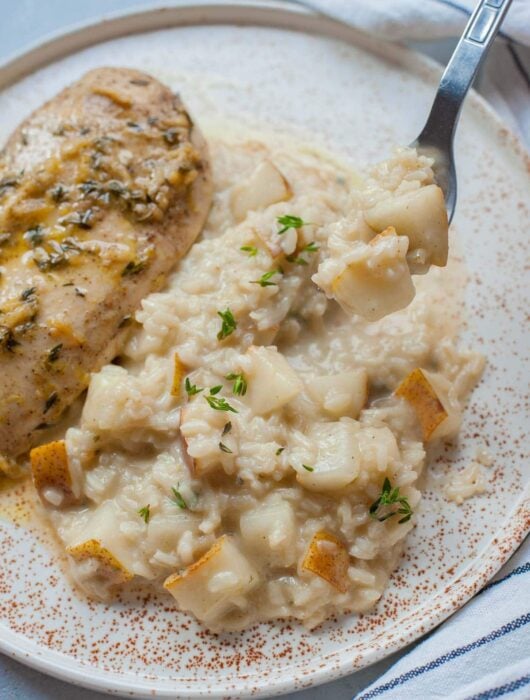 Pear risotto on a white plate with chicken breast on the side.