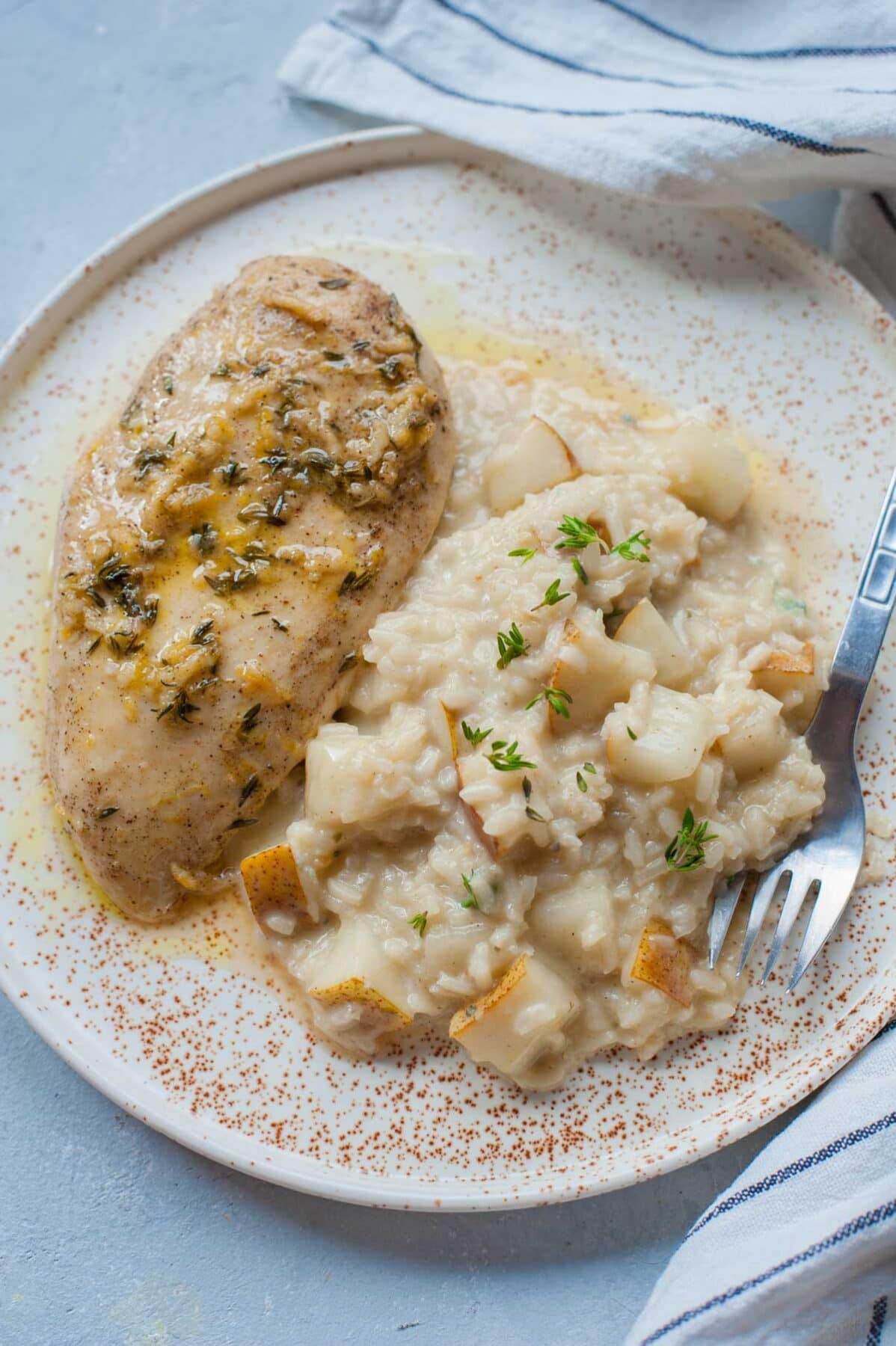 Pear risotto with lemon thyme chicken breast on a white plate.