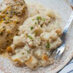 Pear risotto with gorgonzola on a white plate with a side of chicken breast.