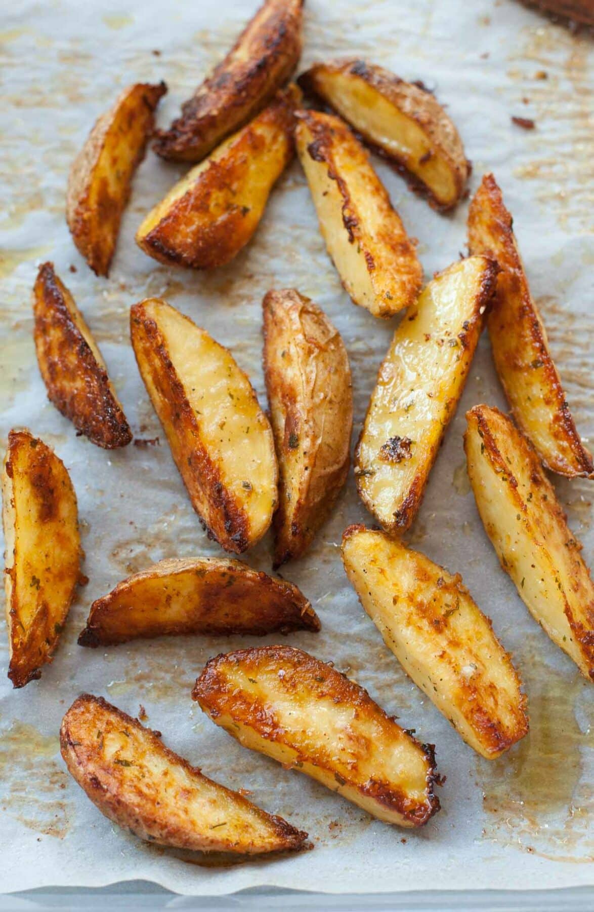 Baked Lemon, parmesan, parsley potato wedges on a parchment paper.